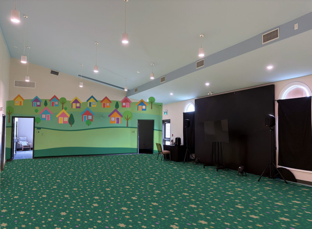 Children's space with painted colourful walls, and a vandalea tile floor of grass and sporadic yellow and purple flowers.